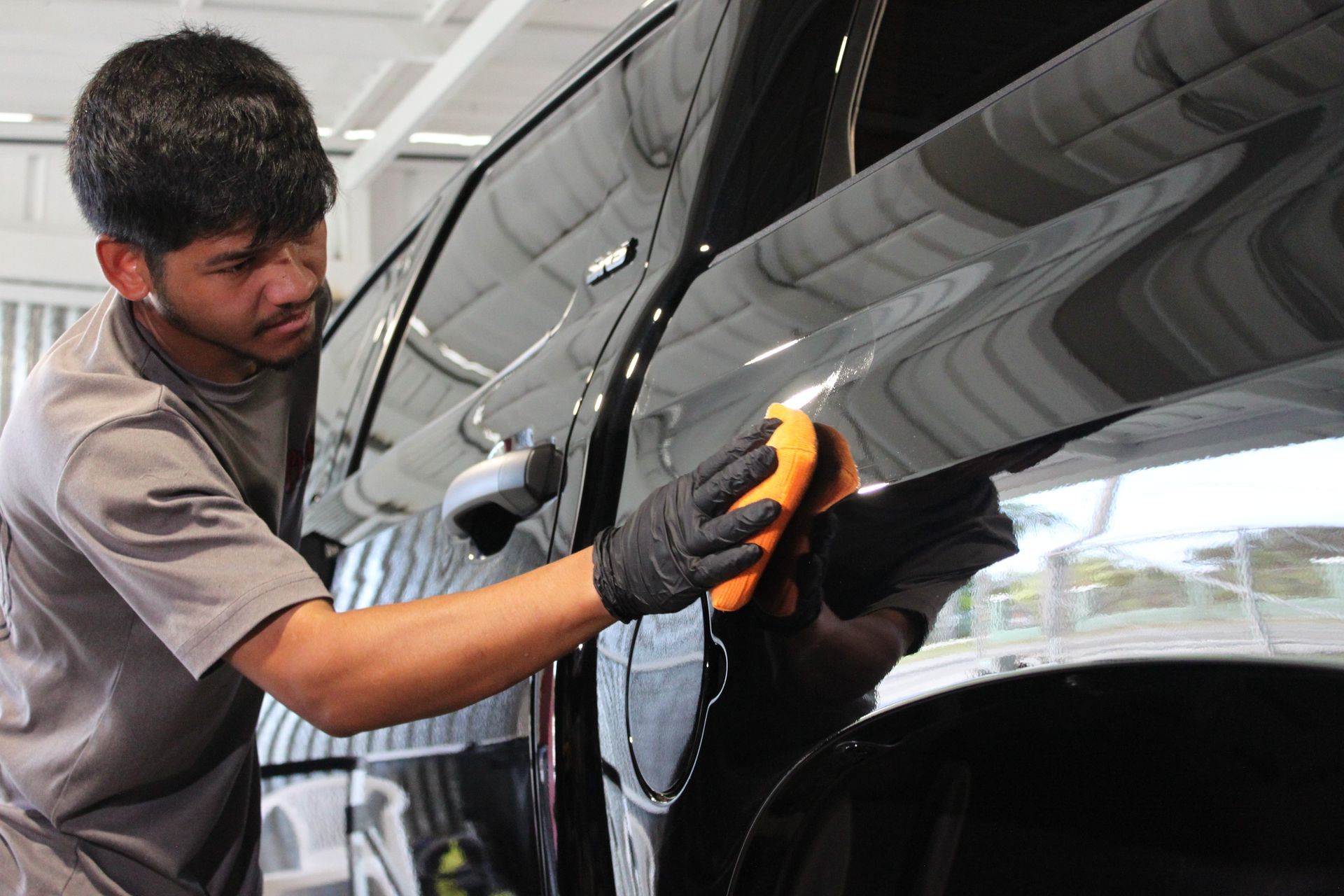 A person wearing black gloves carefully cleans and polishes the side panel of a black car with a yellow cloth.