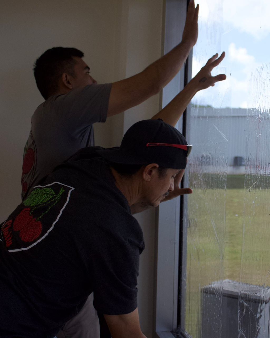 Two people work together to apply or clean a large window, pressing their hands against the glass.