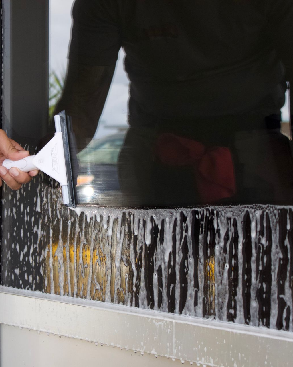 A person uses a squeegee to wipe soapy water down a window pane.