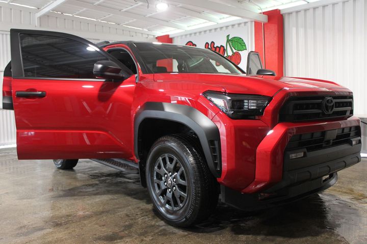 A red Toyota Tacoma pickup truck with its driver-side door open, parked inside a garage.