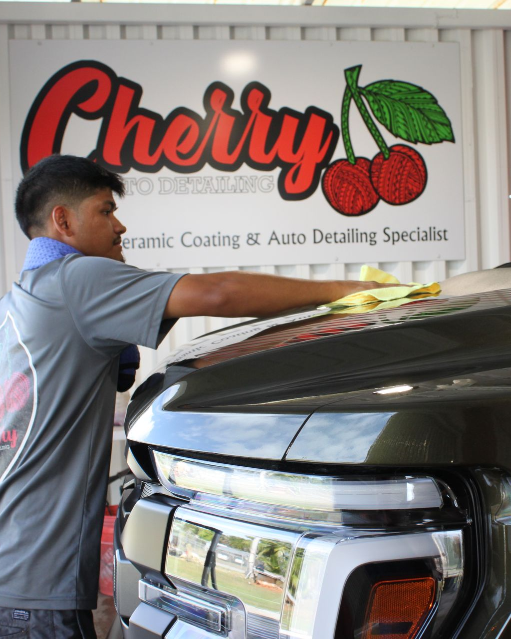 A person wipes down a dark vehicle hood in front of a 