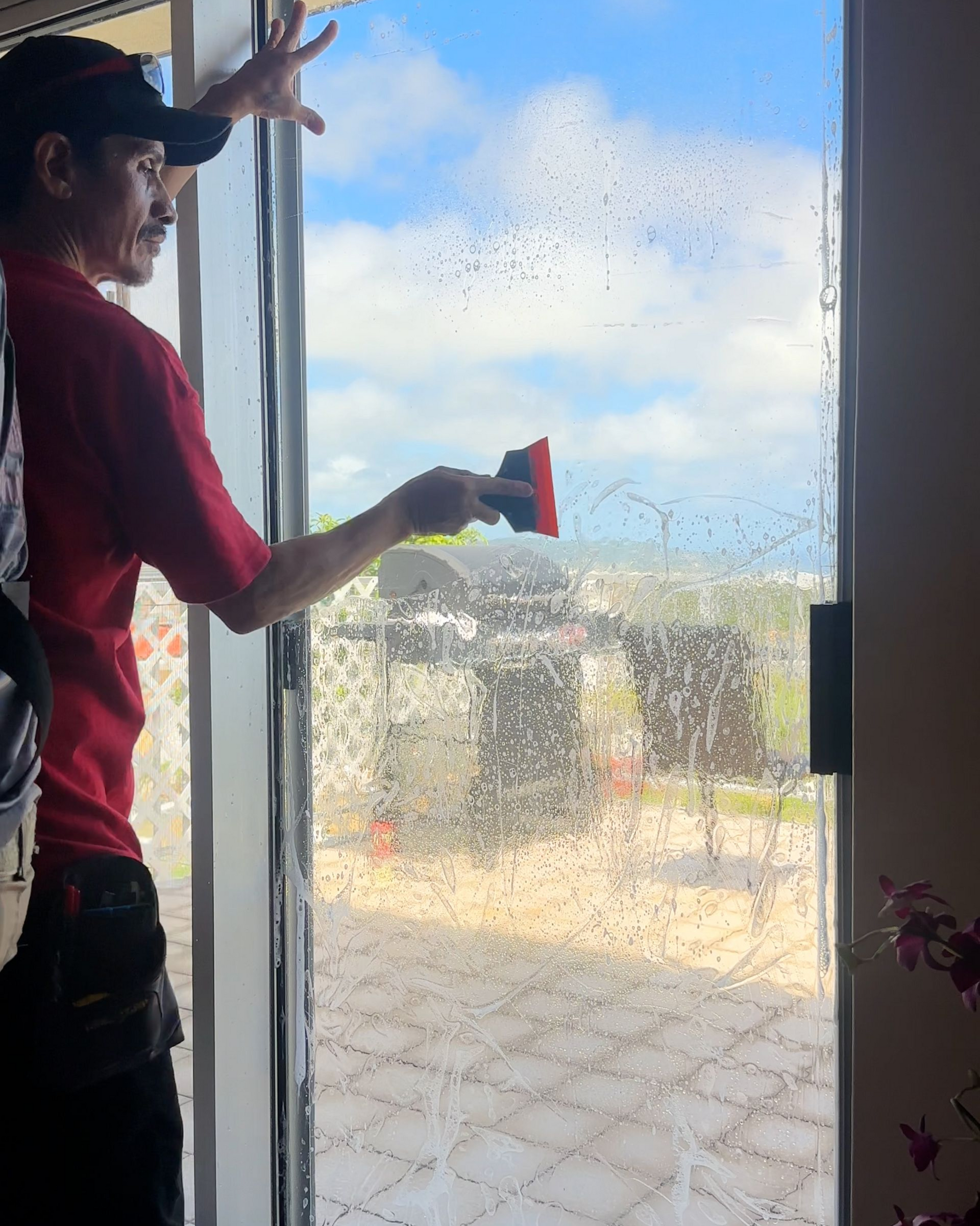 A worker in a red shirt uses a squeegee to apply window film to a glass sliding door.