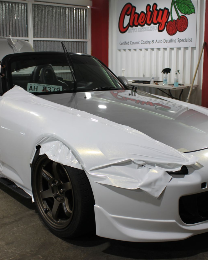 A white sports car parked in an auto detailing shop, partially covered in white protective vinyl wrap.