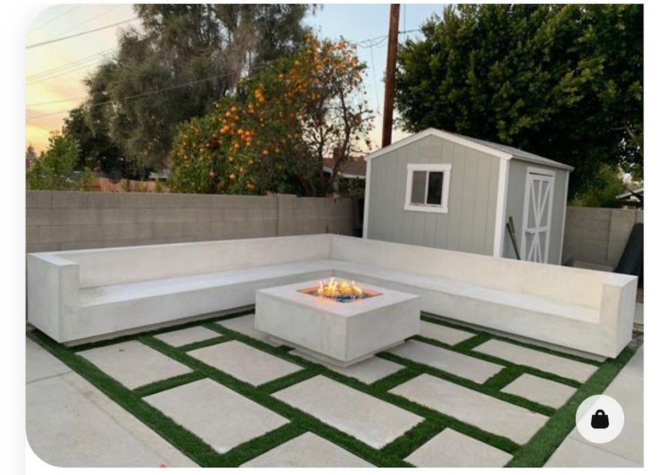 Brown wall next to a building with a white roof and trees.