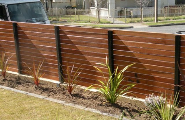 Wooden horizontal plank fence with gravel and greenery next to a sidewalk.