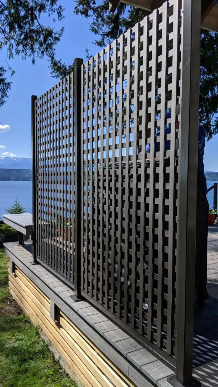 Dark gray lattice privacy screen in front of water and sky.