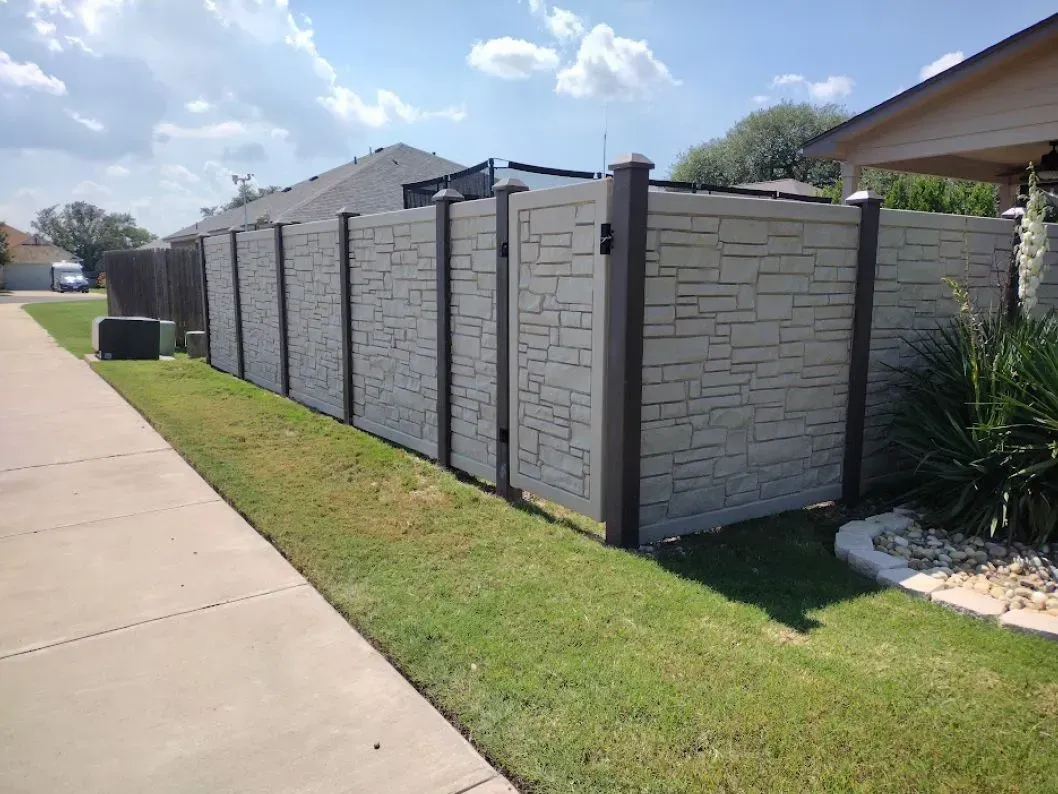 Tan textured privacy fence with dark brown posts bordering a green lawn and sidewalk.