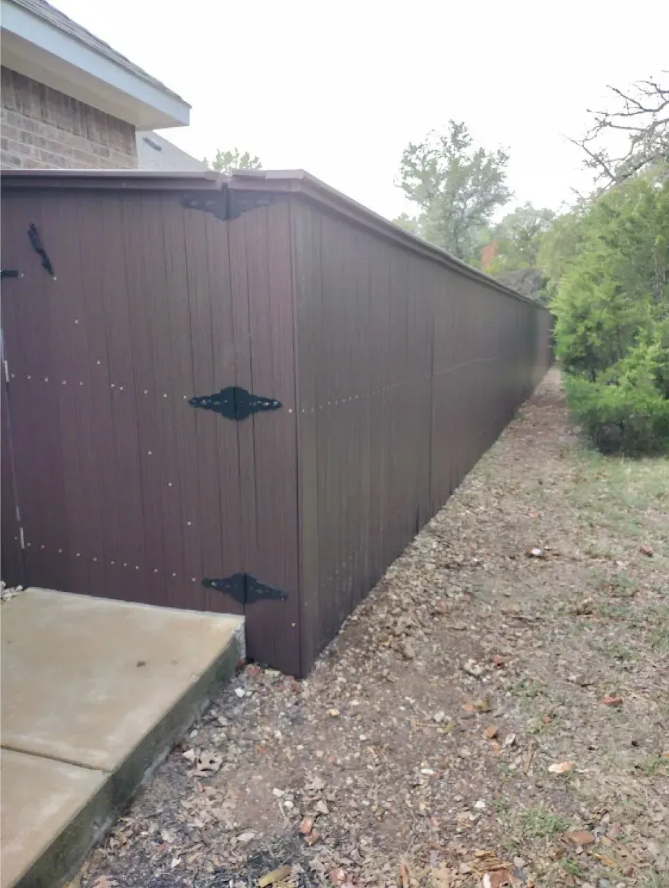 Brown wooden fence next to a brick house and grassy area.