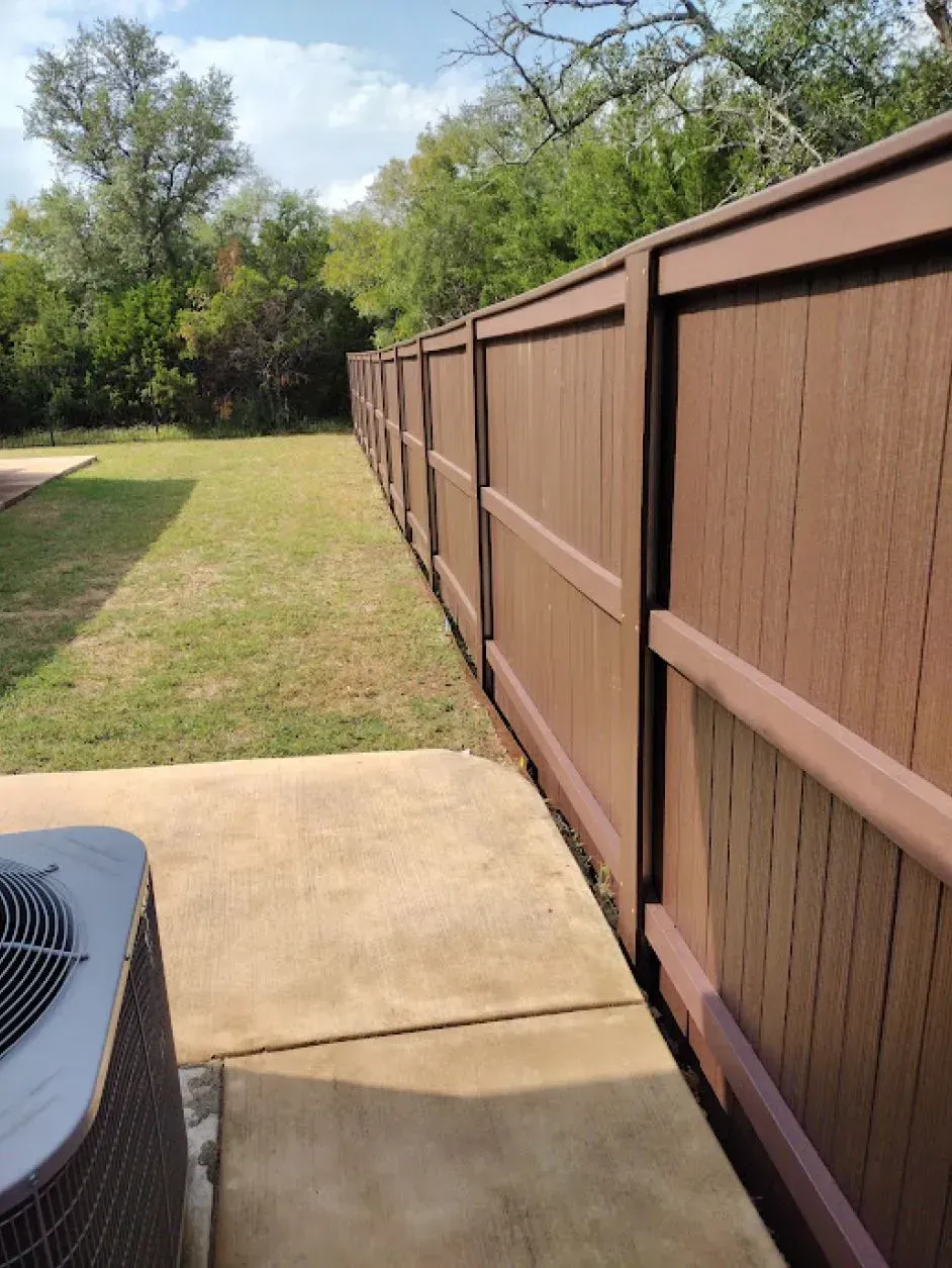 Brown fence bordering a backyard with green grass, a concrete patio, and an air conditioning unit.