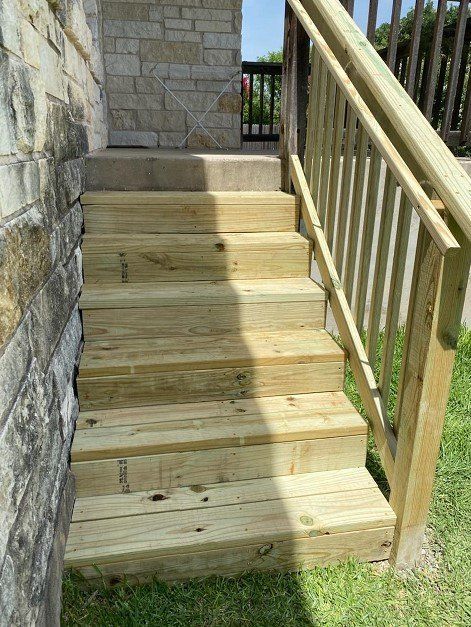 Wooden outdoor steps with a railing, leading to a stone wall and door.