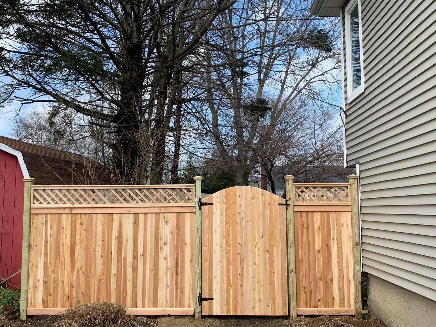 Wooden fence with gate, red shed, and beige house on a cloudy day.