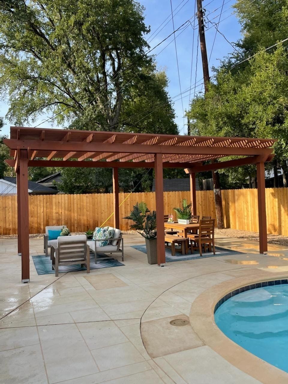 Pergola over patio furniture near a pool; wood, blue, and tan colors.