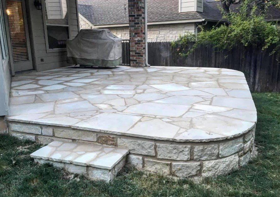Stone patio with a curved retaining wall and step in a backyard.