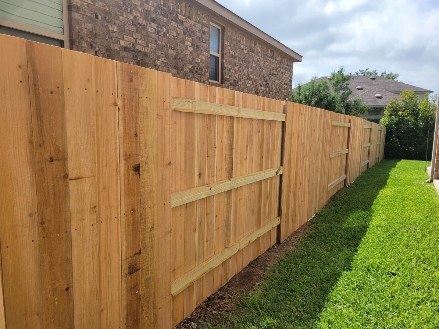 Wooden fence along a grassy lawn, with a brick house in the background.