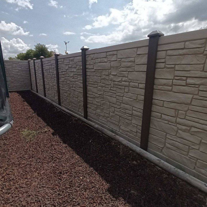 Stone-textured concrete fence with brown posts and caps in a yard with brown mulch.