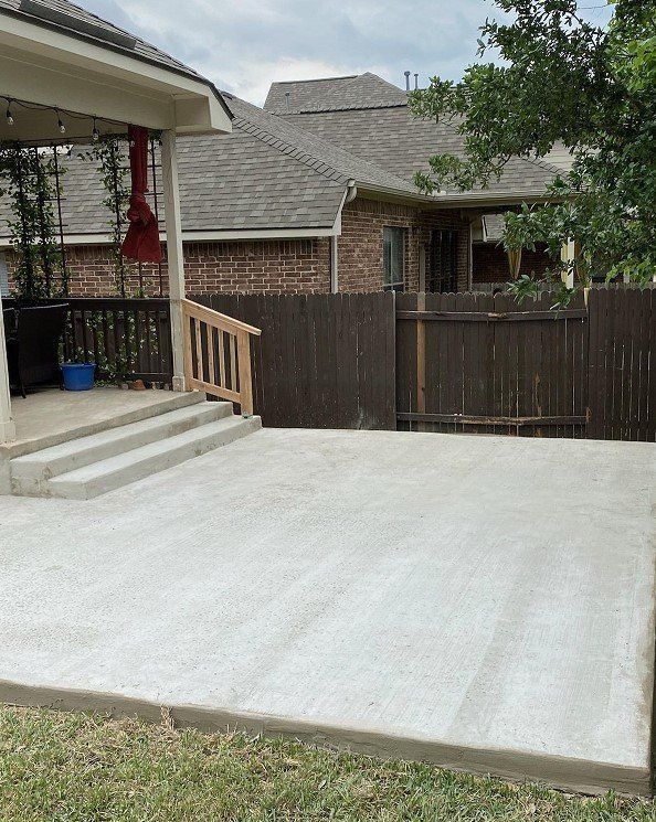 Concrete patio with steps leading to a porch; brown fence surrounds yard.