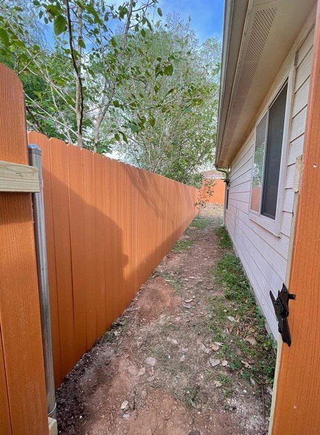 Narrow dirt path between a brown fence and a white house.