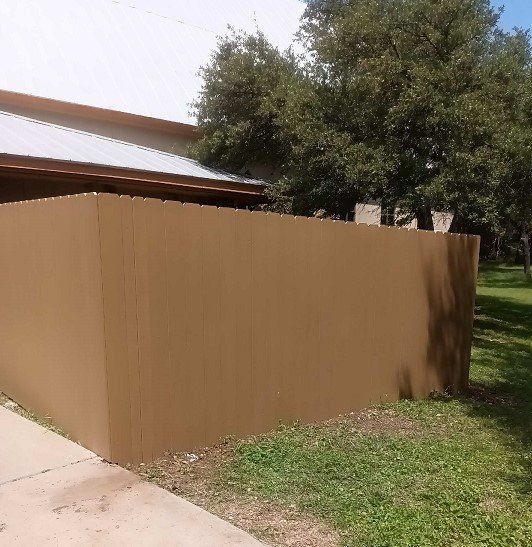 Brown fence in front of a building with a metal roof, alongside green grass.