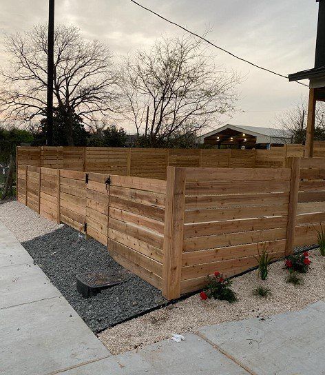 Wooden horizontal plank fence with gravel and greenery next to a sidewalk.