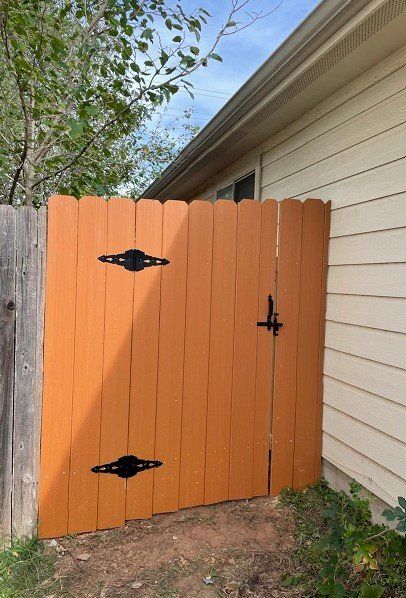 Orange wooden gate attached to a beige house. Black hinges and latch.