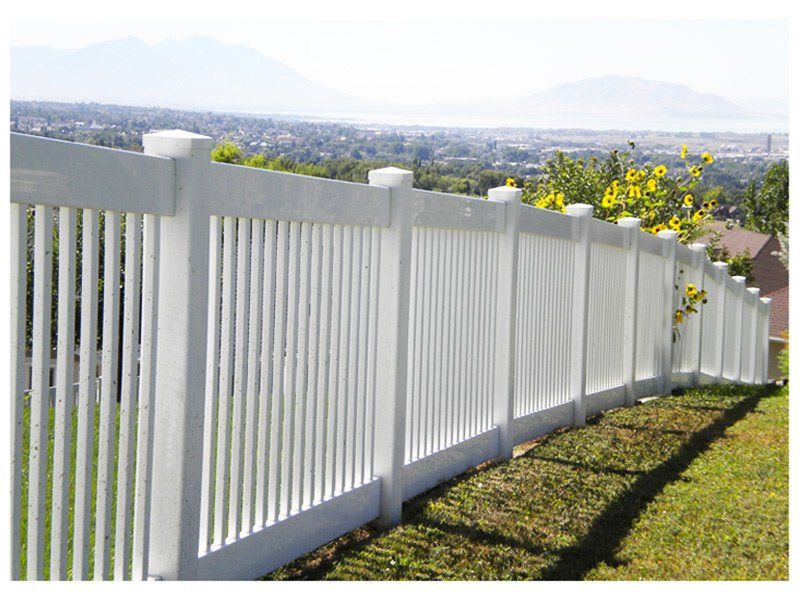 White picket fence on a grassy hill, overlooking a distant city and mountains on a sunny day.