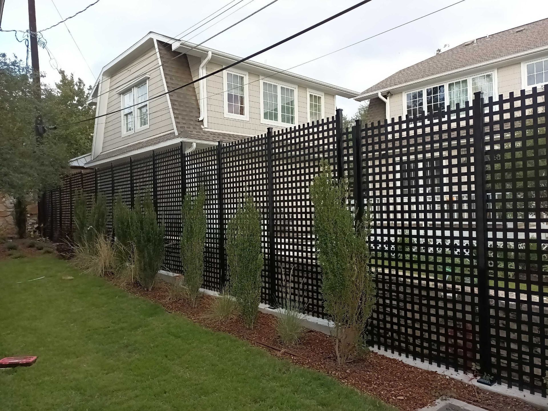 Black lattice fence along a lawn, bordering a house with visible windows.