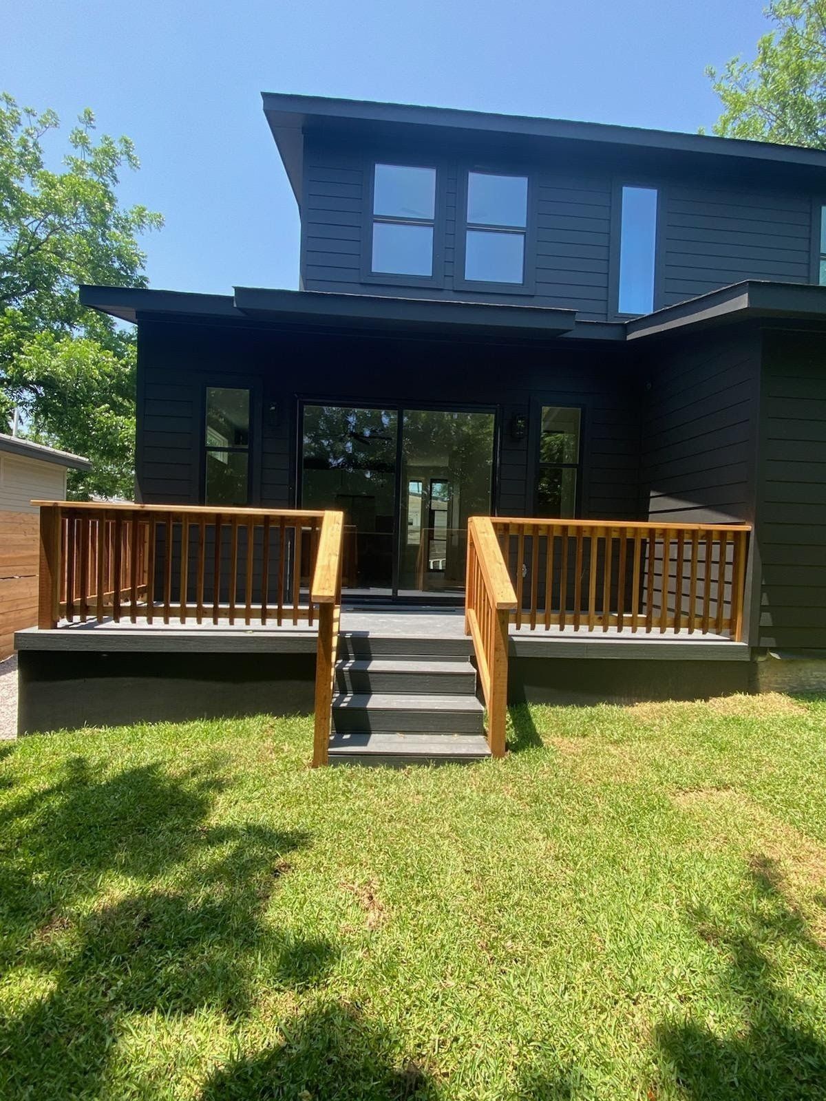 Black house with a wooden deck and stairs leading down to a grassy yard.