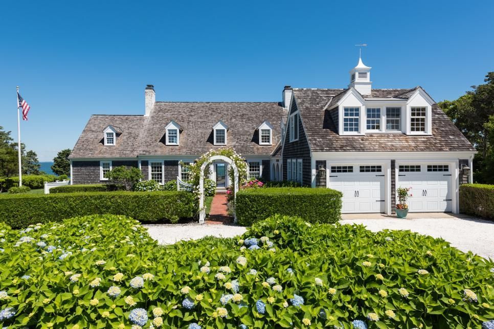 House with white garage doors, dormers, and a shingle roof, with a manicured garden.