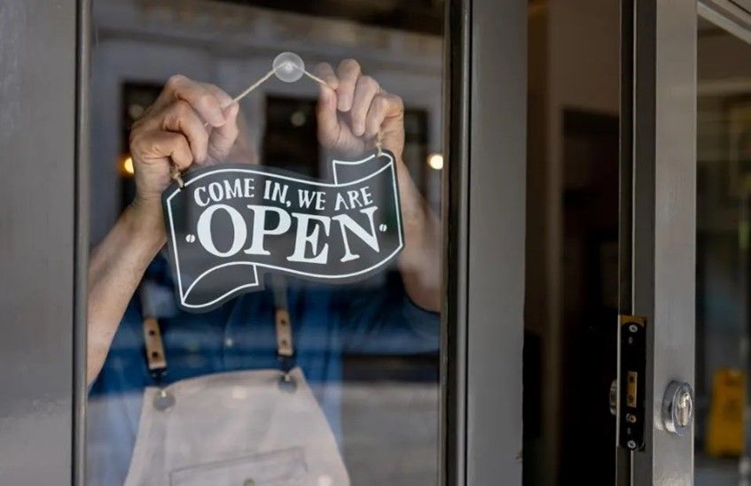 Person hanging a white “We are open” sign on a glass door.
