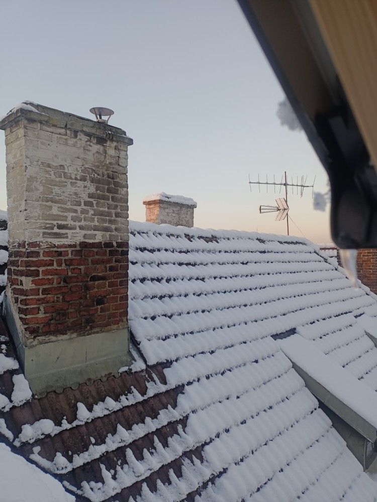 Snow-covered rooftops with chimneys against a light sky.