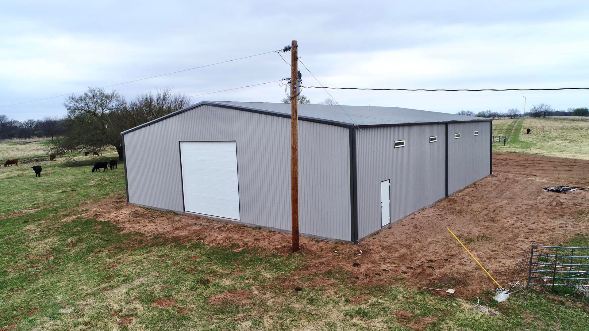 A large metal building is sitting in the middle of a field next to a power pole.
