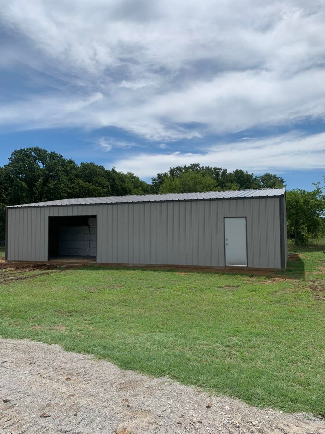 A gray metal building with a white door is in the middle of a grassy field.