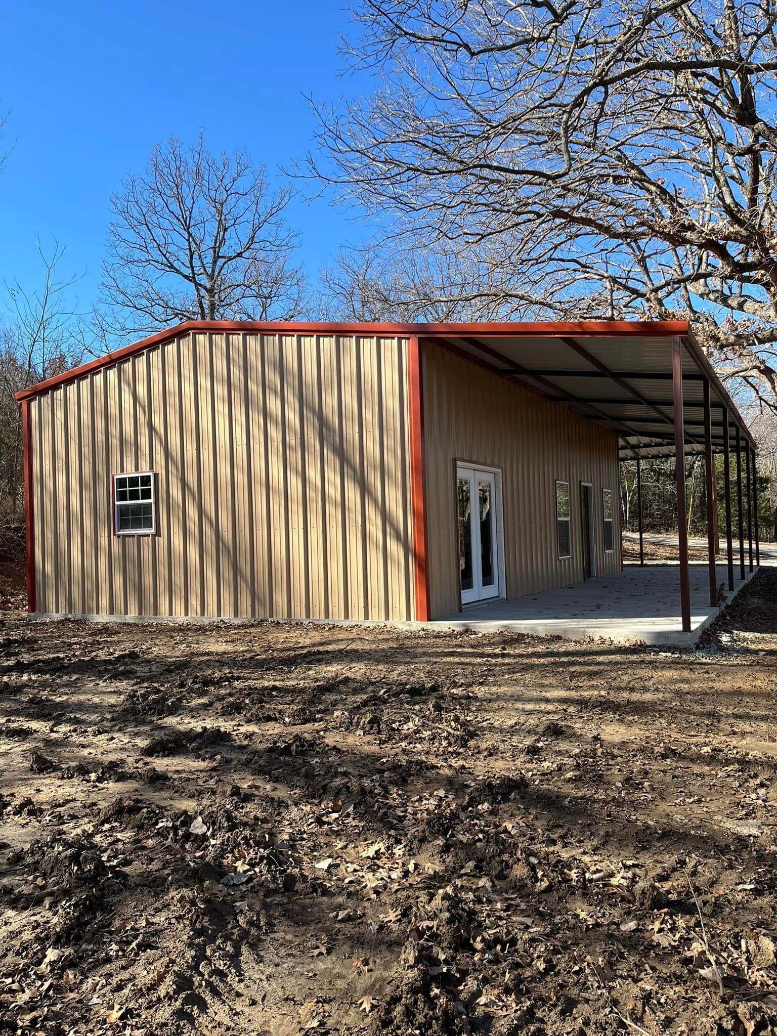 A metal building with a porch is sitting in the middle of a dirt field.