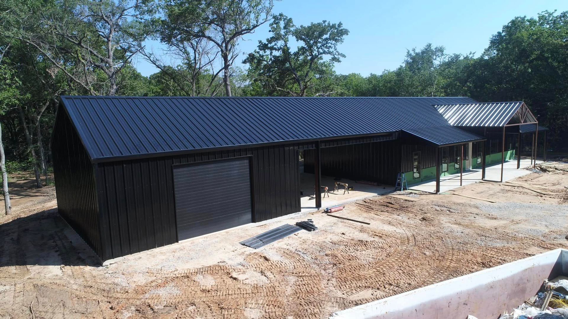 A large black building with a black roof is sitting in the middle of a dirt field.