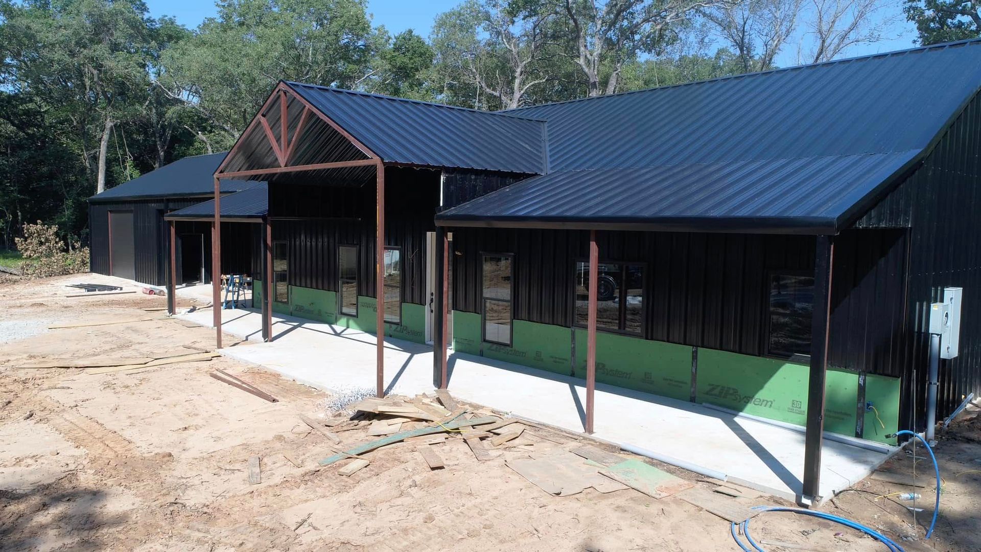 A house with a black roof is being built in a dirt field.