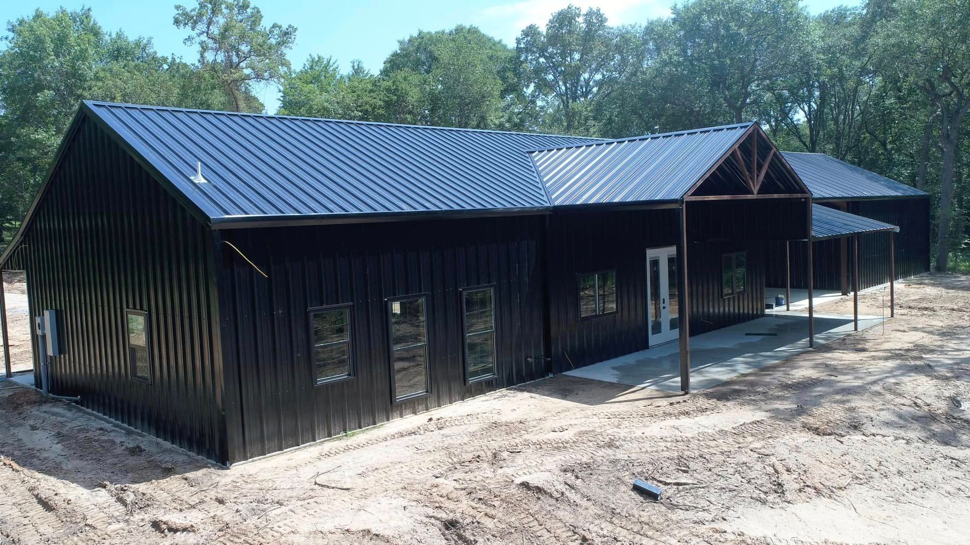 A large black building with a metal roof is in the middle of a dirt field.