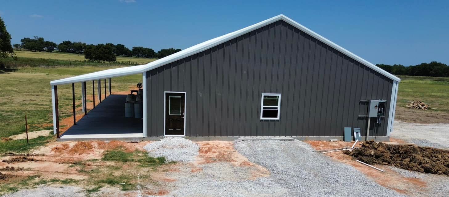 A large barn with a porch and a driveway in a field.