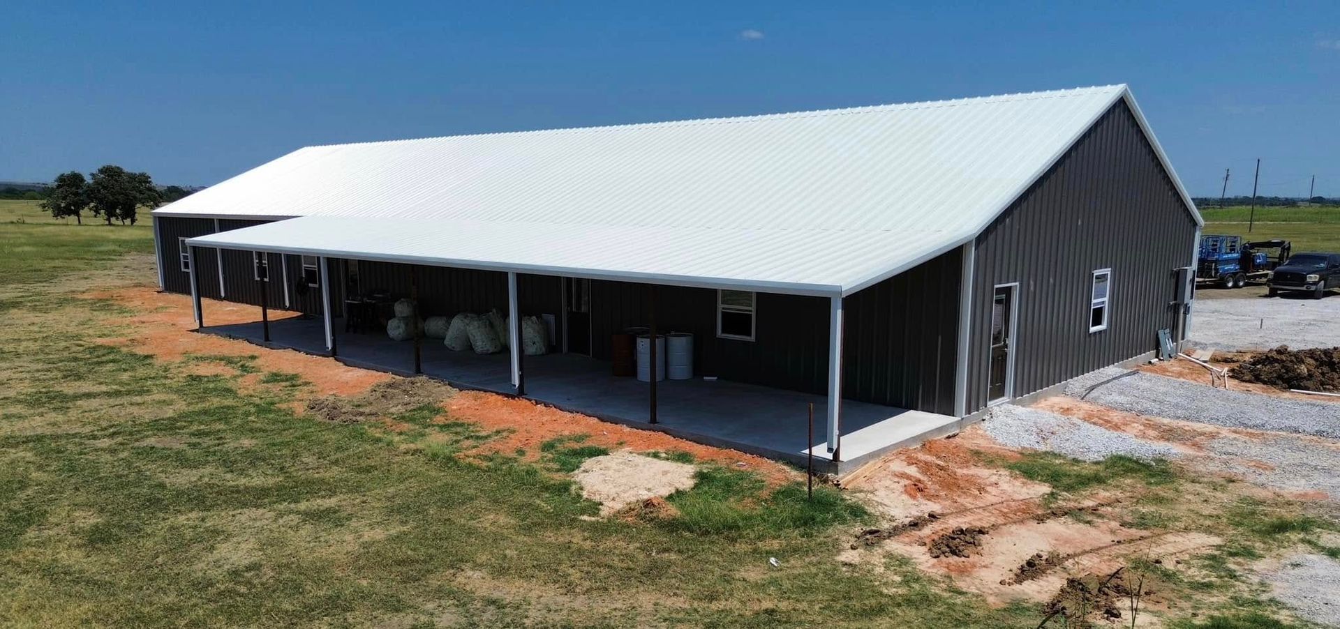 A large metal building with a white roof is sitting in the middle of a grassy field.