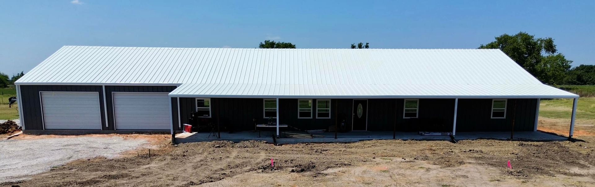 A black house with a white roof is sitting in the middle of a dirt field.