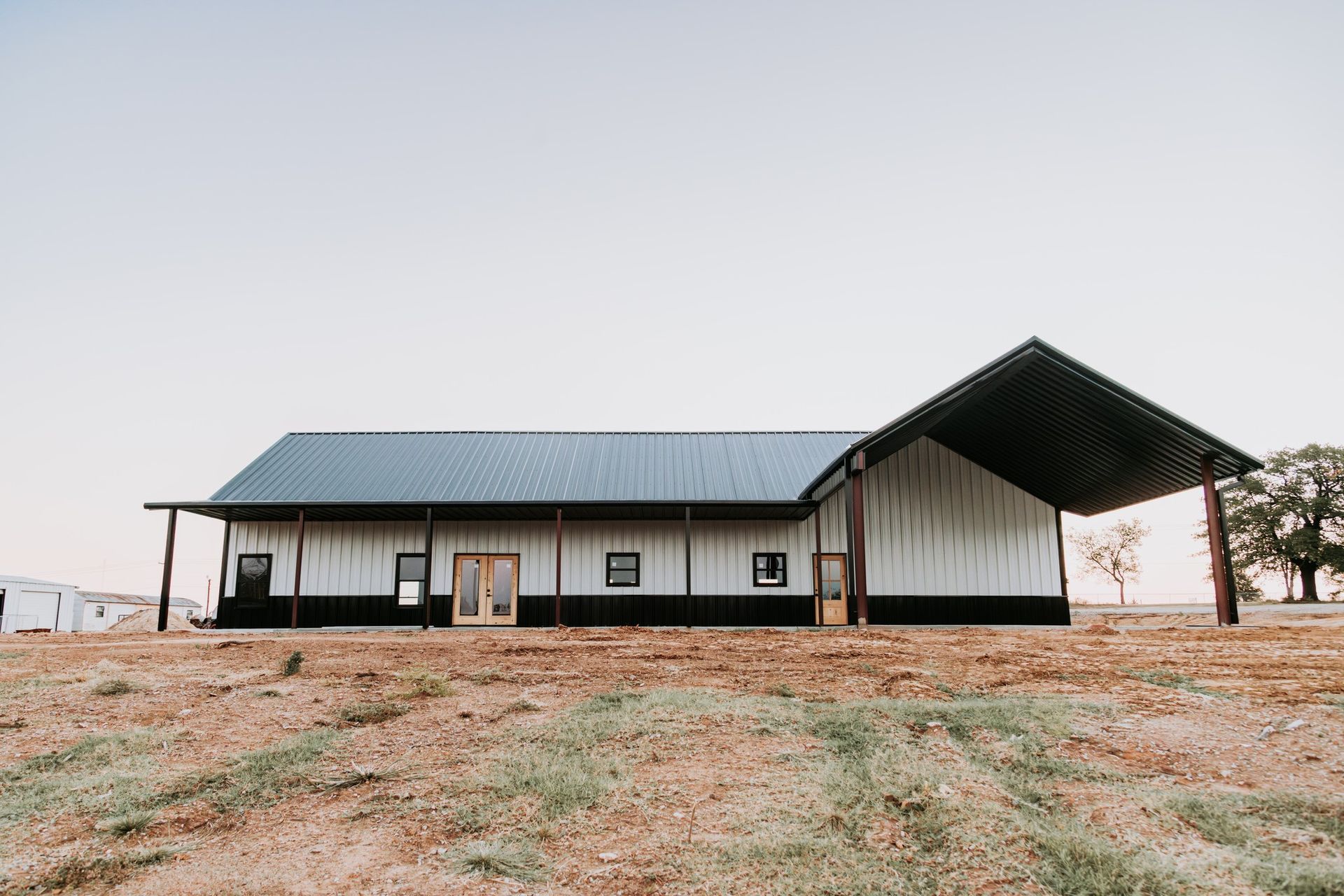 A large white barn with a black roof is sitting in the middle of a field.