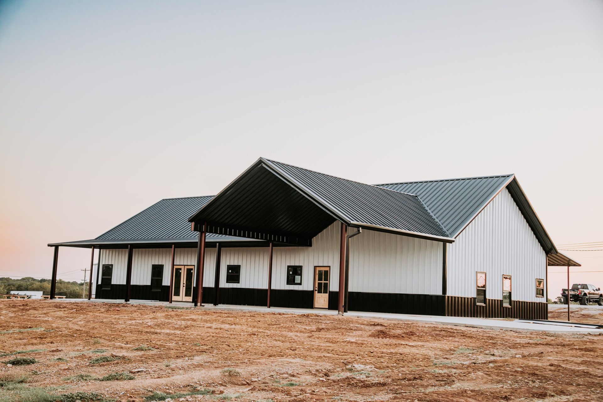 A large white and black barn is sitting in the middle of a dirt field.