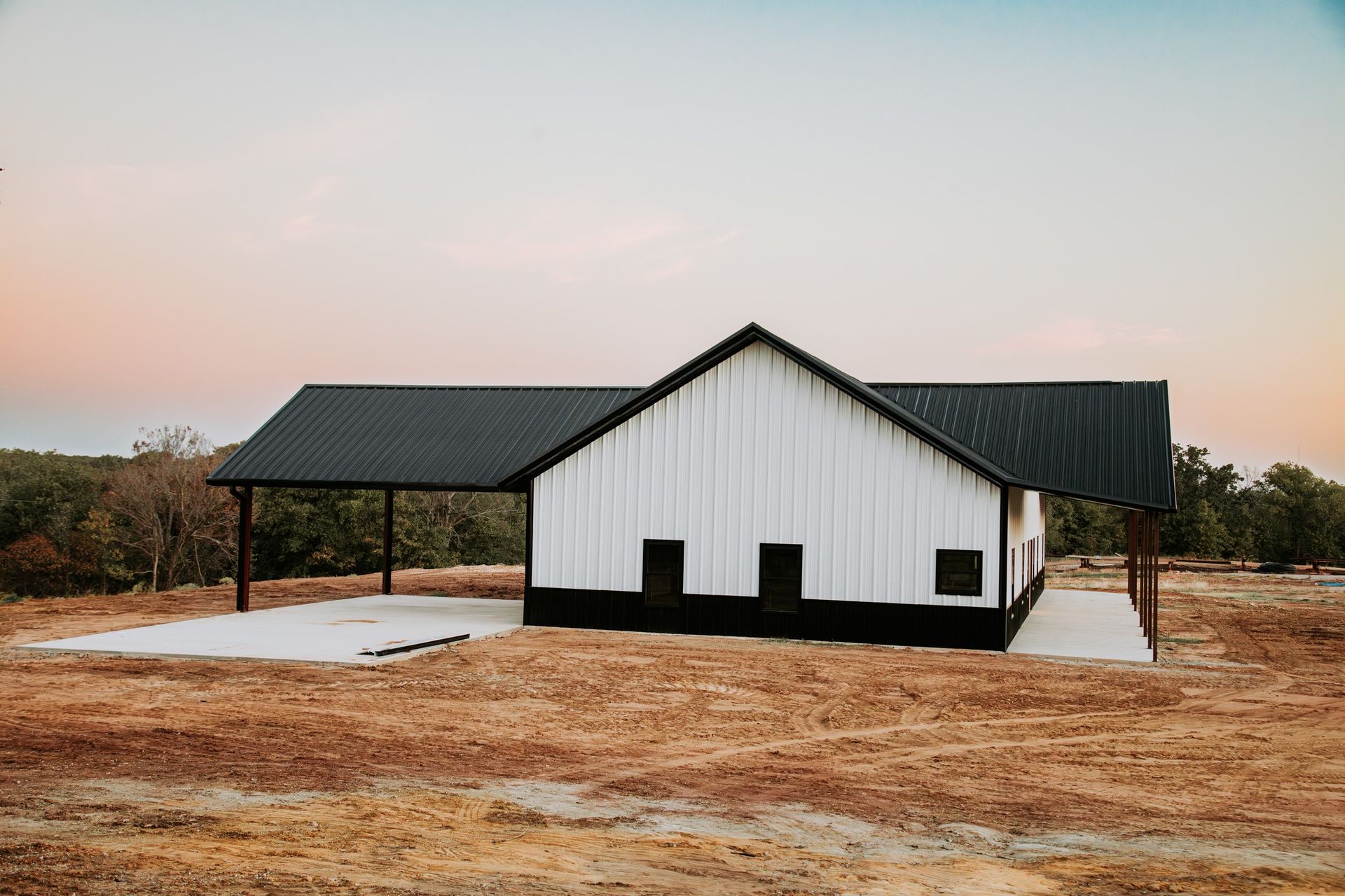 A white and black barn is sitting in the middle of a field.