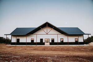 A large white building with a black roof is sitting in the middle of a dirt field.