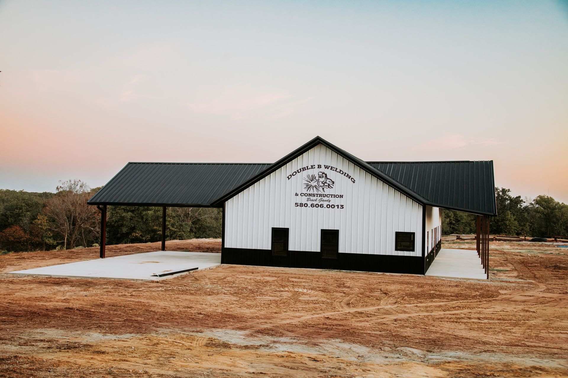 A white barn with a black roof is sitting in the middle of a field.