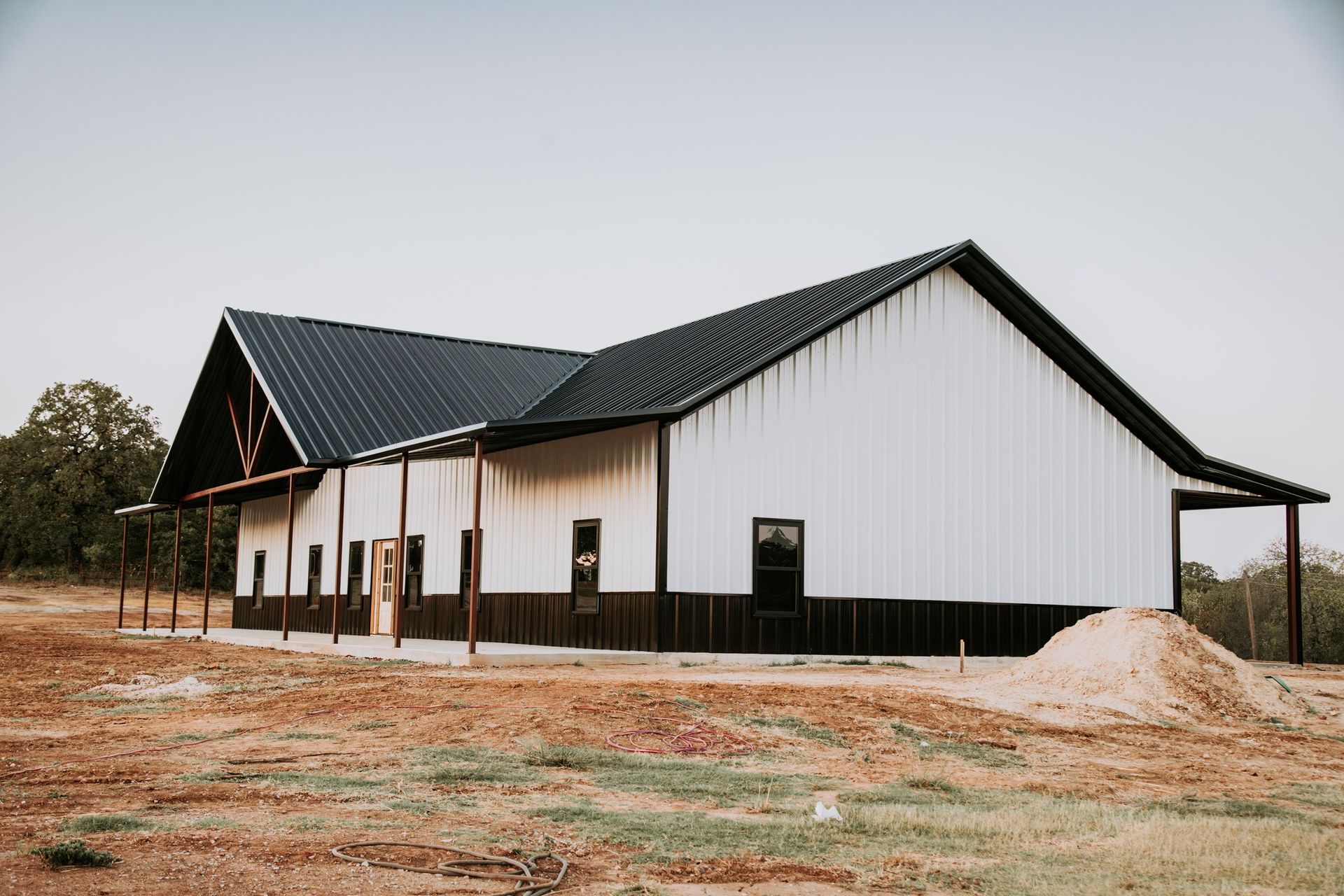 A large white building with a black roof is sitting in the middle of a dirt field.