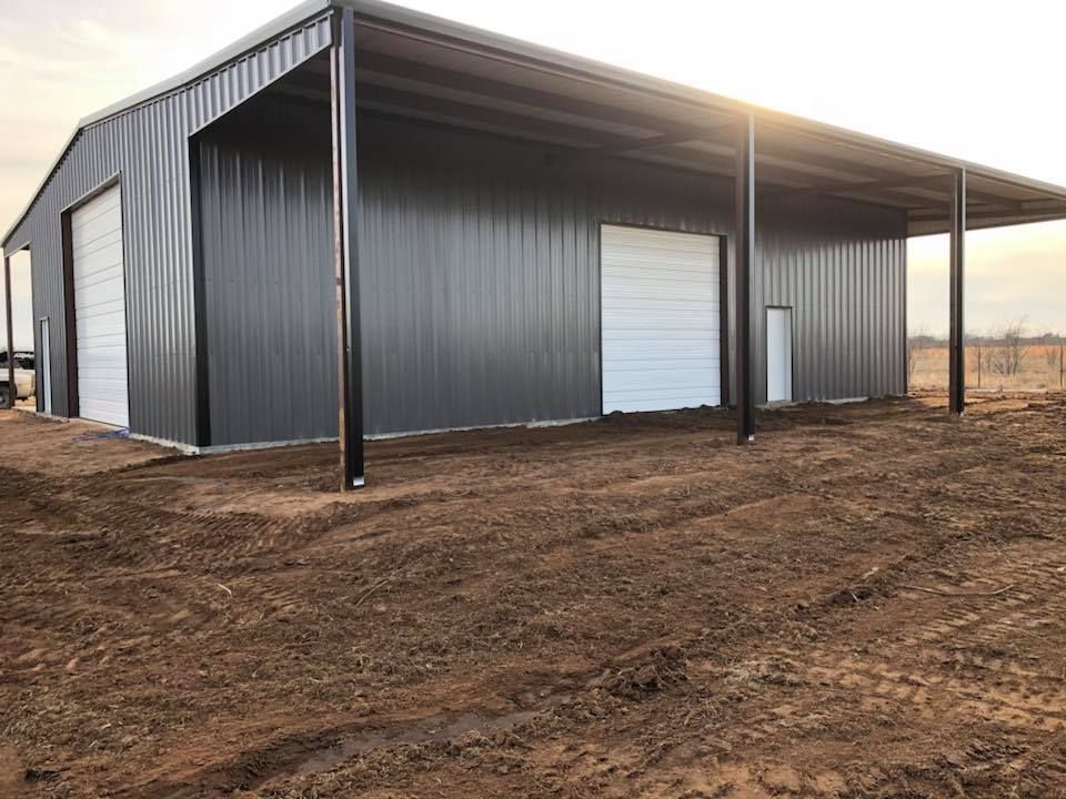 A large metal building with a white door is sitting in the middle of a dirt field.