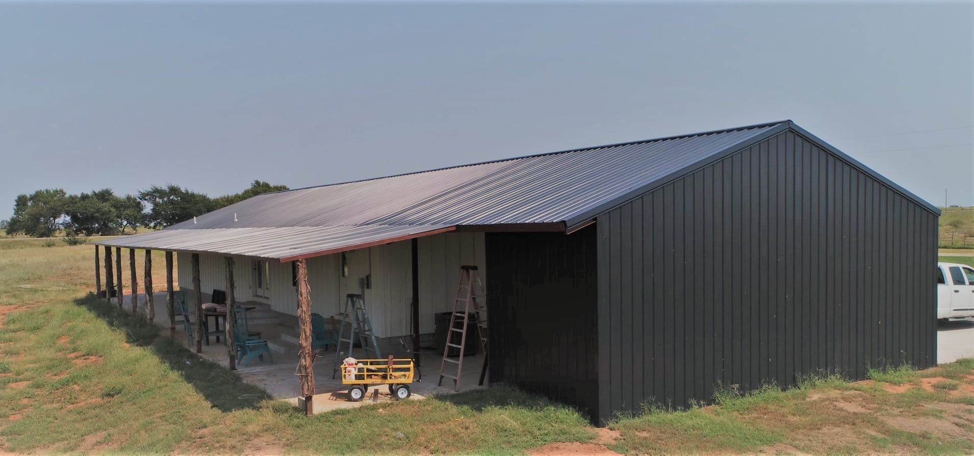 A large black metal building with a porch in the middle of a field.