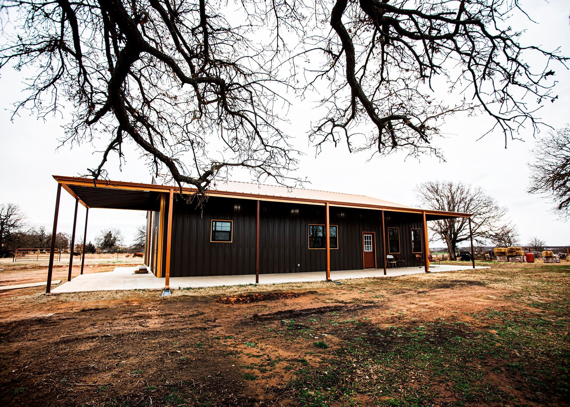 A black house with a porch is sitting in the middle of a field.