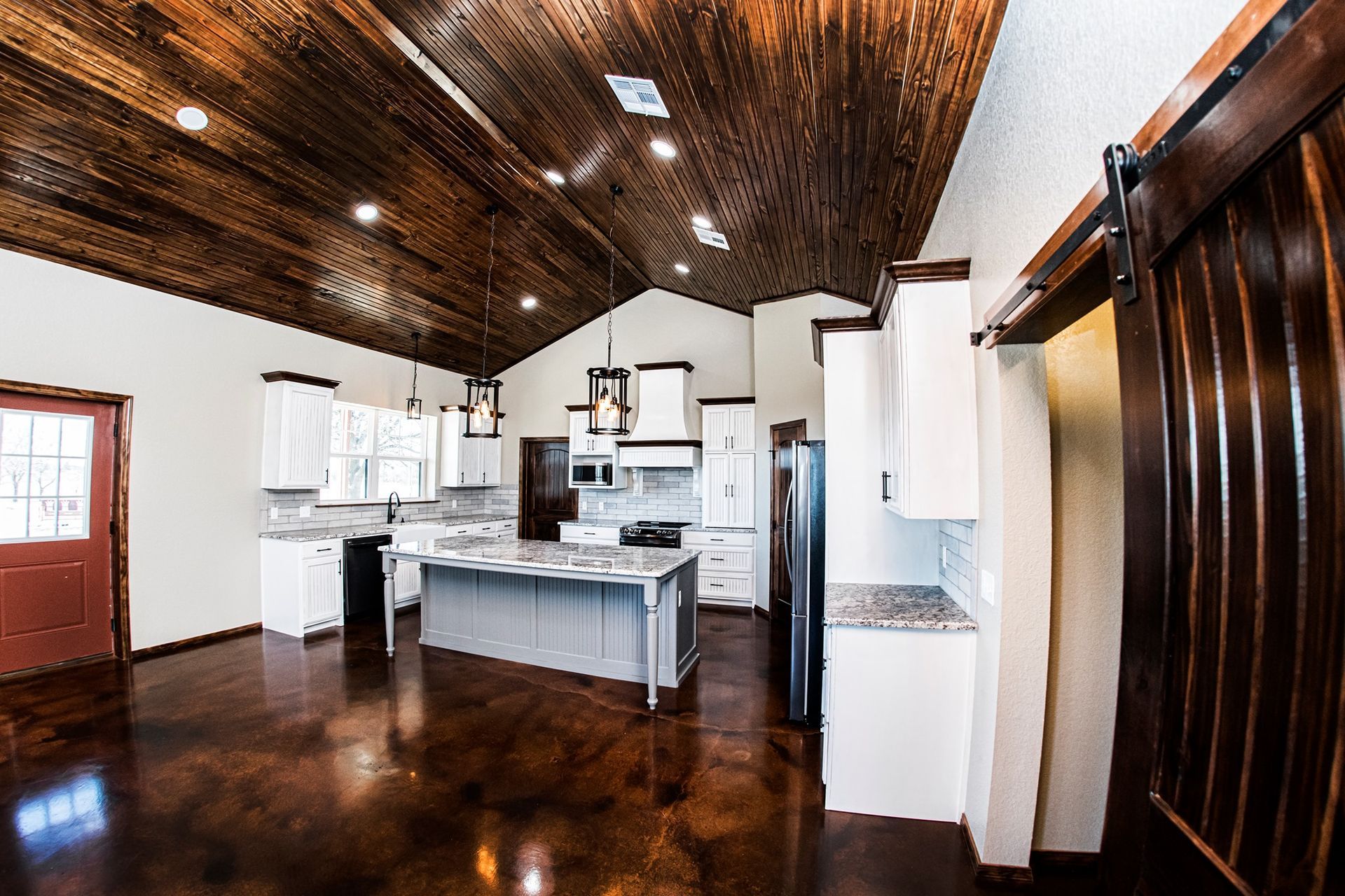 A kitchen with a wooden ceiling , white cabinets , and a large island.