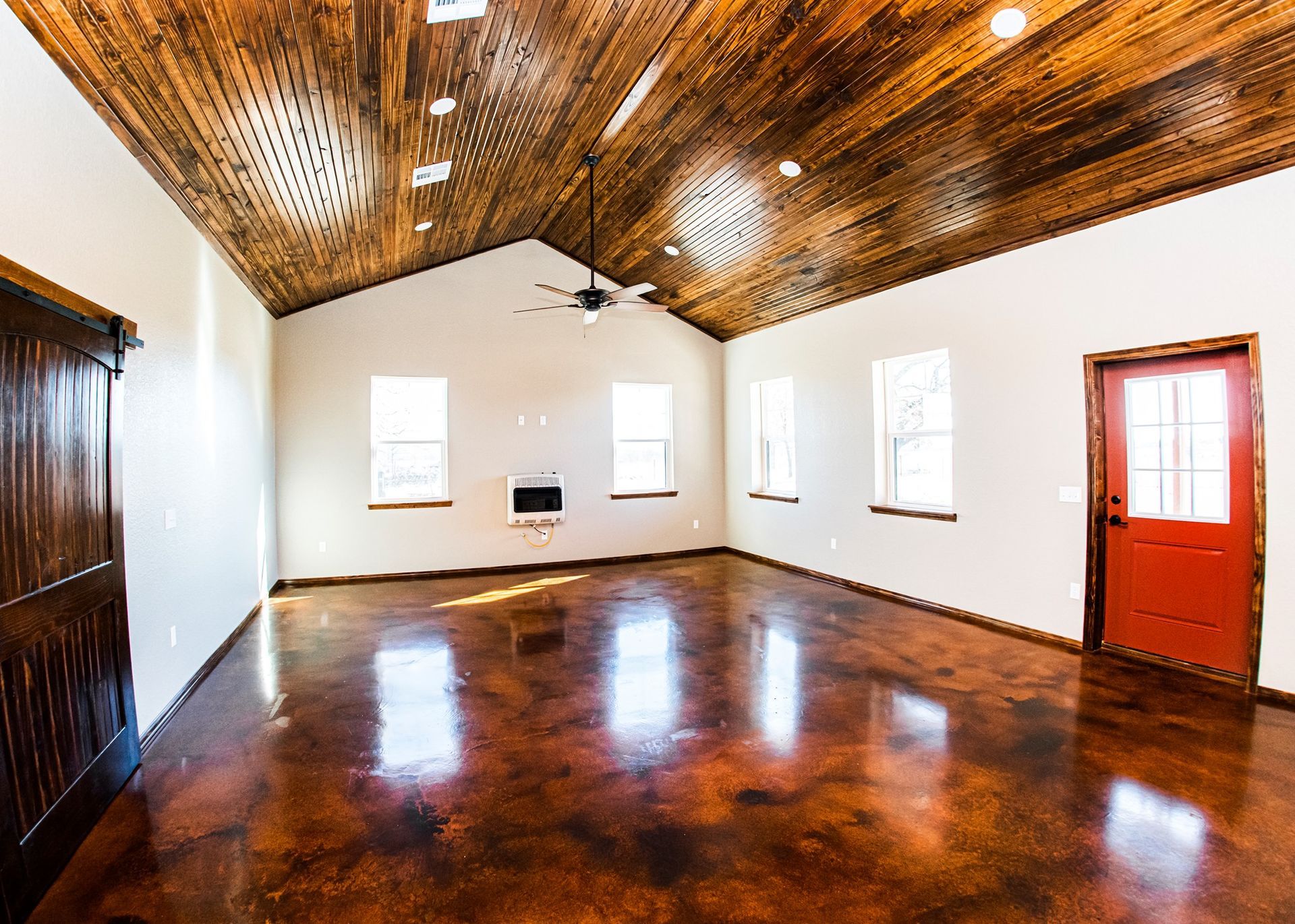 A large empty room with a wooden ceiling and a red door.